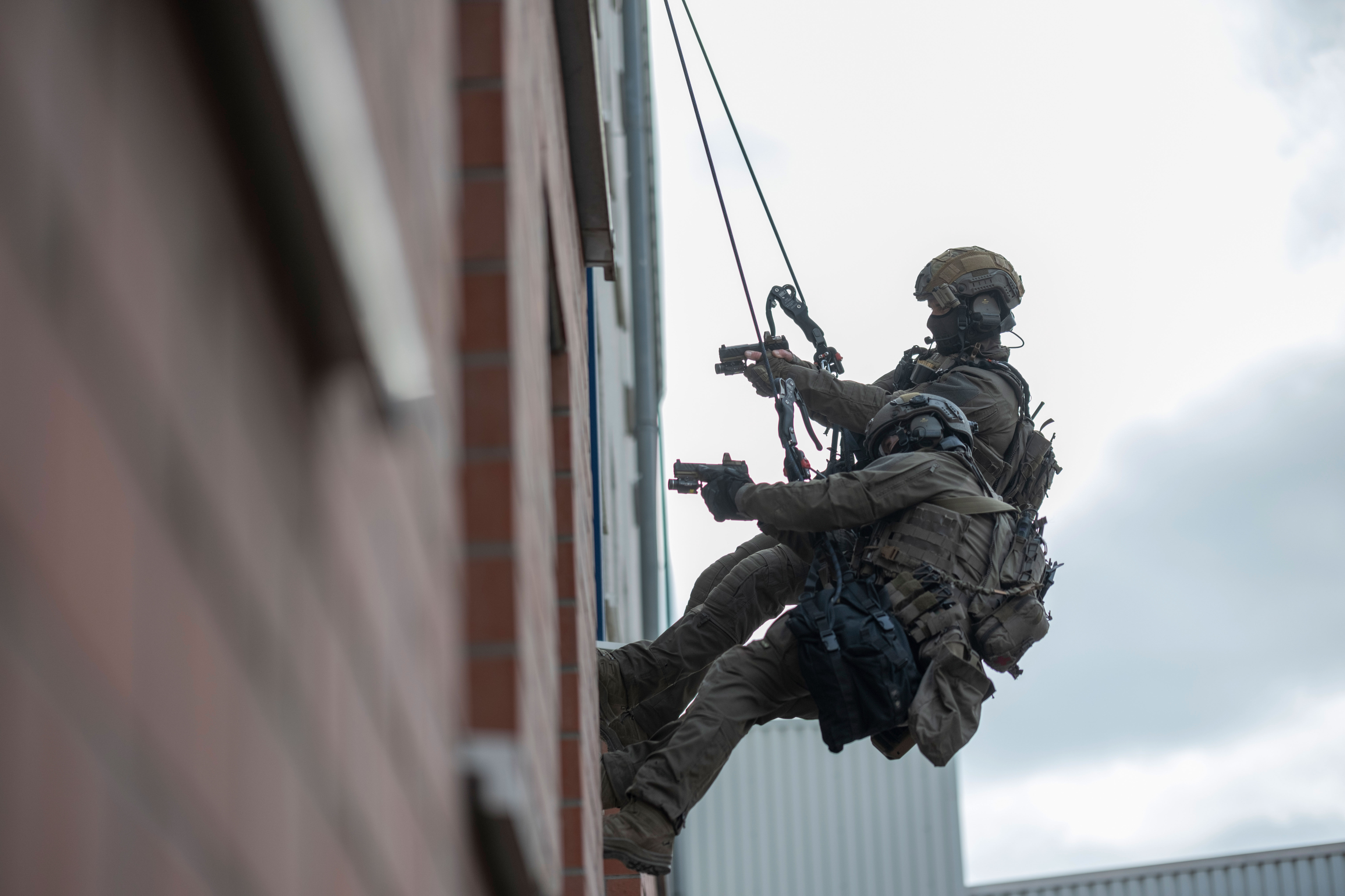 Zwei SEK-Beamte des Klettertrupps seilen sich außen an einer Hauswand in ein Fenster ab. Sie halten ihre Waffen in den Raum gerichtet.