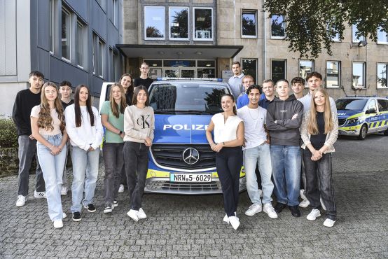 17 junge Frauen und Männer rund um einen Streifenwagen der Polizei